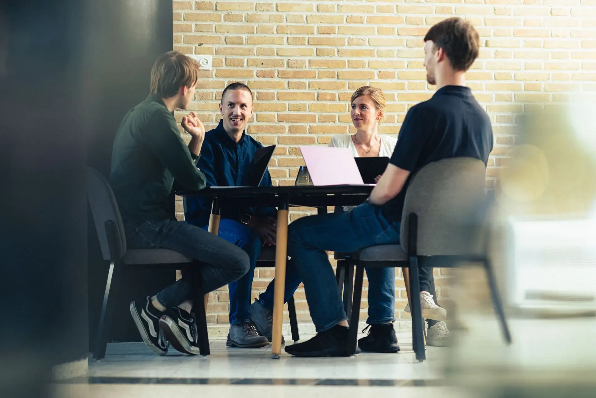 Vier Codeforward-collega's overleggen aan tafel voor een bakstenen muur
